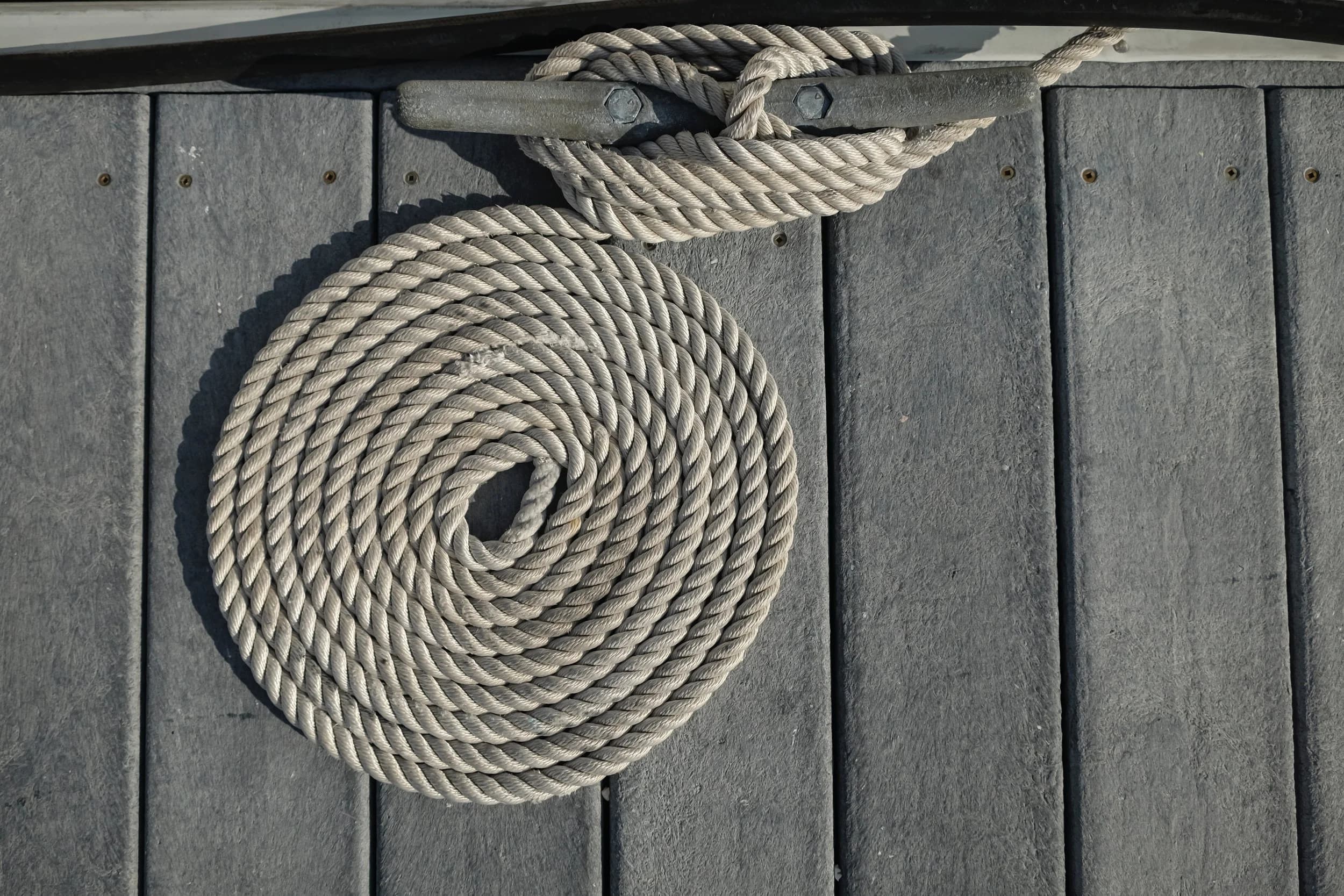 A coiled dock line at a cleat on the grey decking of the docks